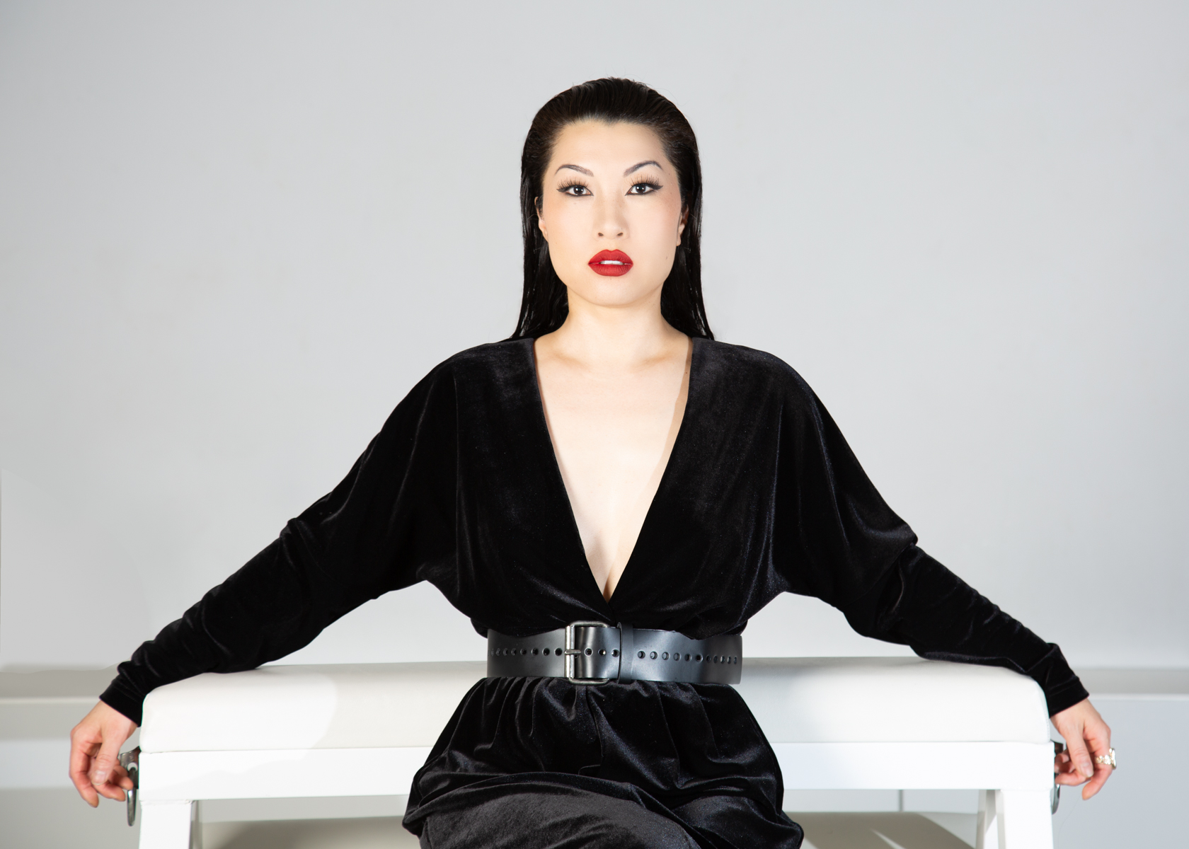 a person wearing a black dress with slicked back black hair seated against a white background