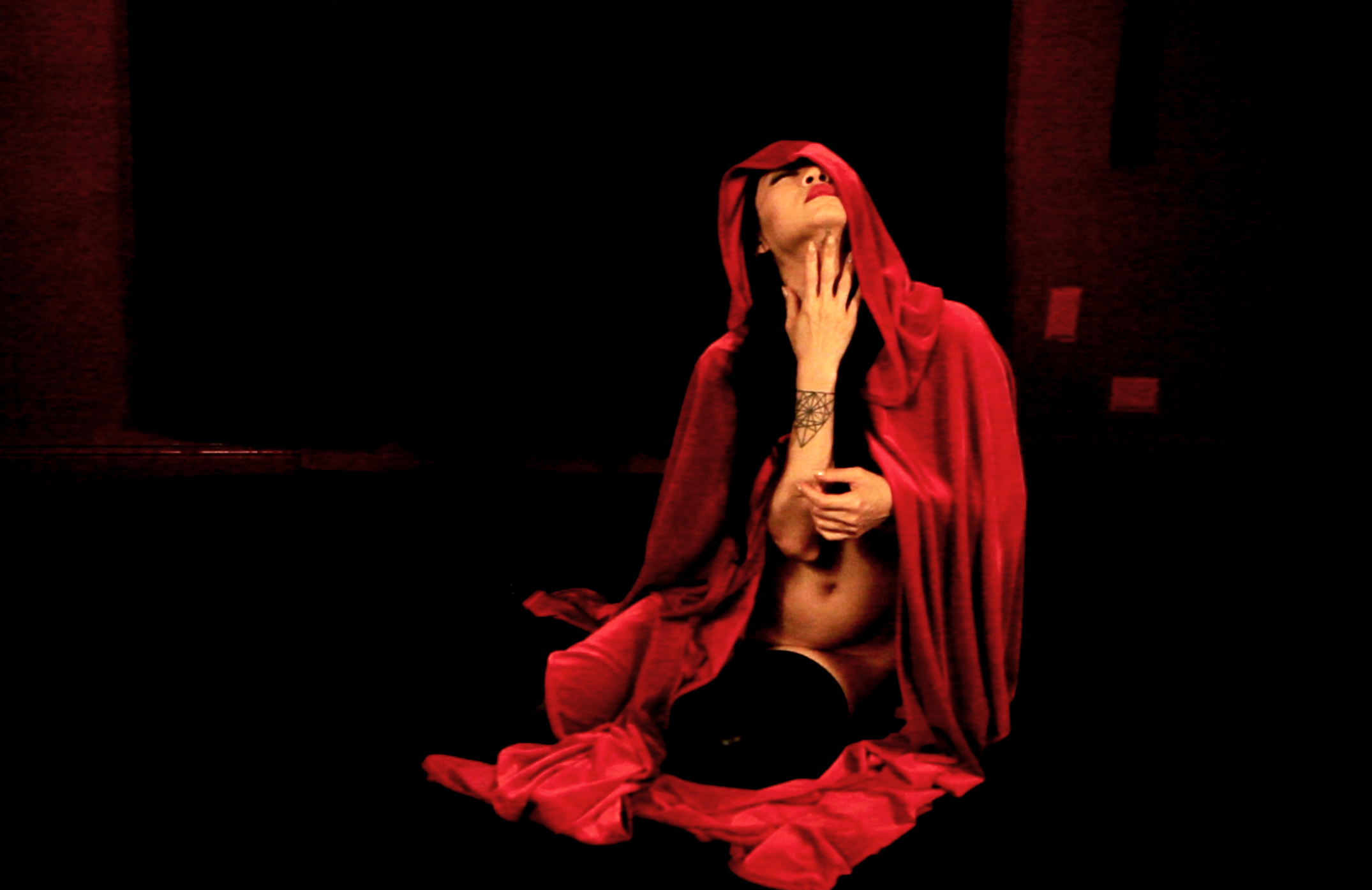 a person against a black background seated and draped in red fabric